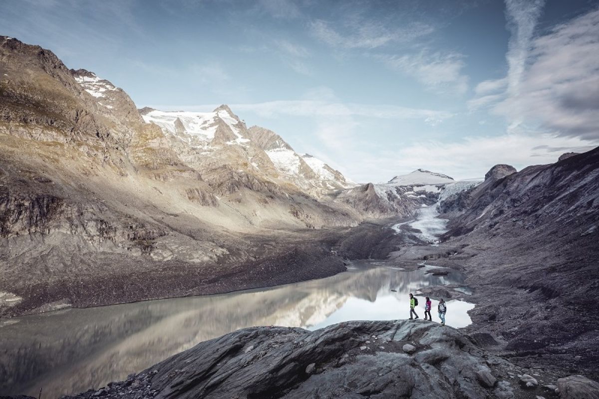 3 Menschen stehen vor einem See mit Blick auf Berge