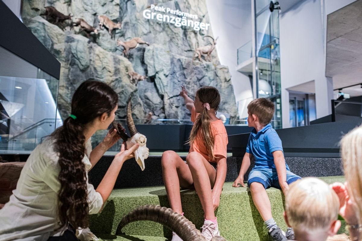 2 Kinder sitzen mit Frau vom Nationalpark vor einer Steinwand mit Steinböcke