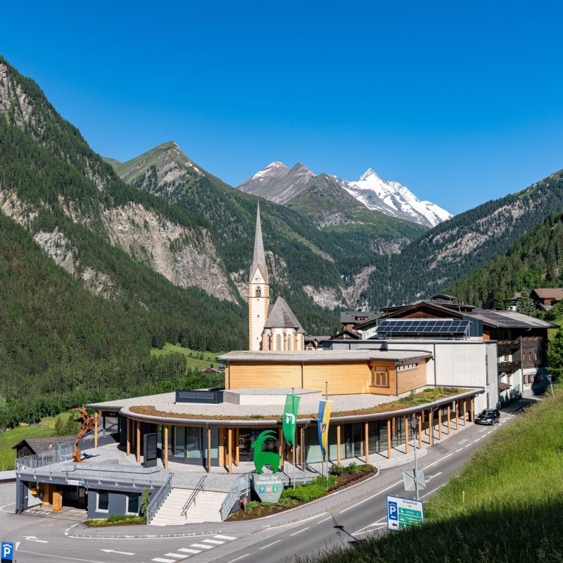 Außenaufnahme im Sommer von Haus der Steinböcke. Die Kirche im Hintergrund vor blauem Himmel